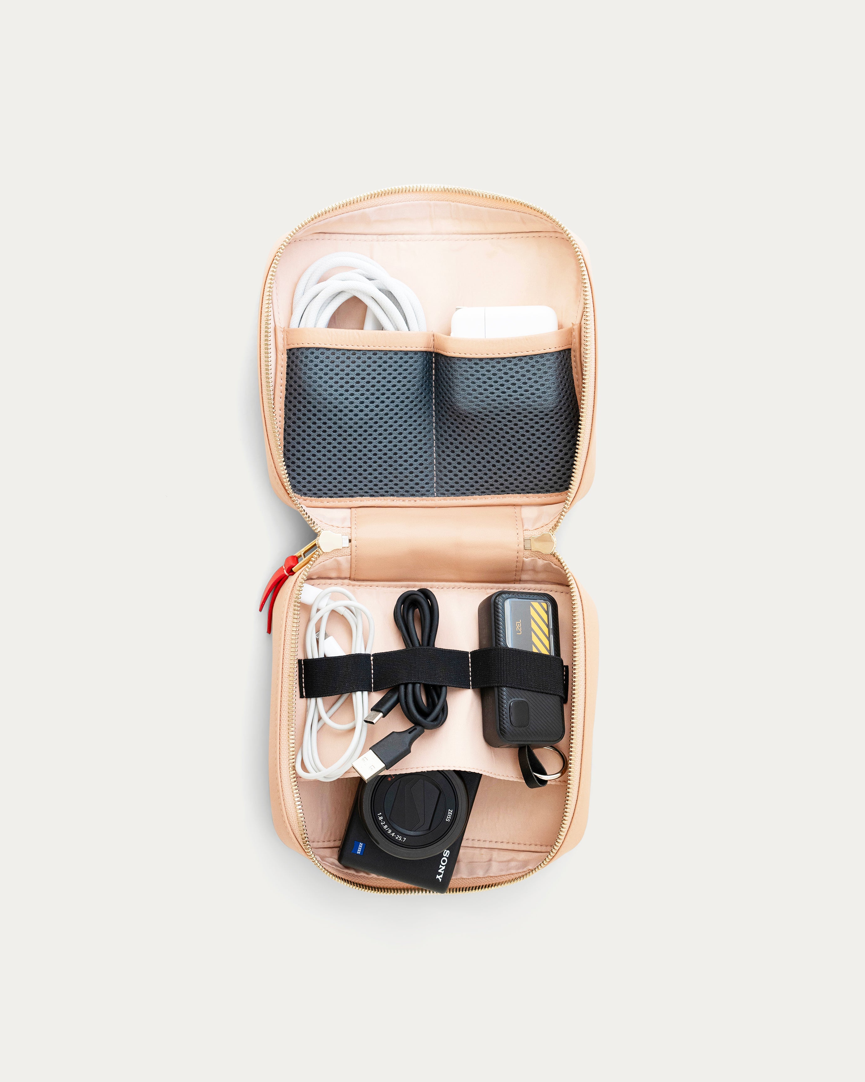 Open beige travel organizer with electronic accessories on a light gray background